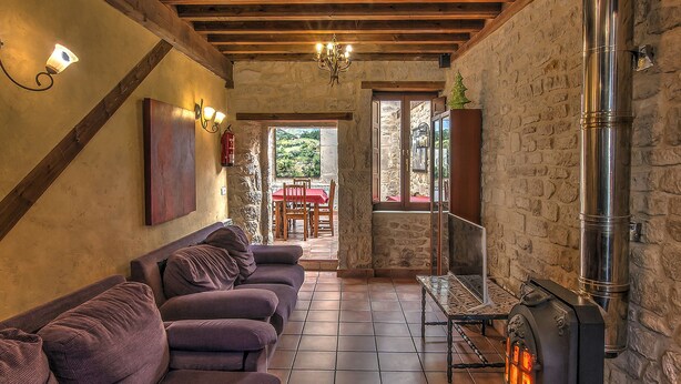 A cozy room with a stone fireplace, wooden beams, and a sofa.