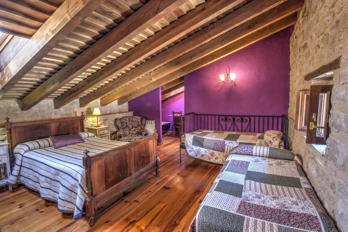 A rustic bedroom with exposed wooden beams, a wooden bed, a small table, and a purple wall.
