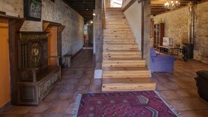 A wooden staircase in a rustic interior with stone walls, a patterned rug, and a blue armchair.