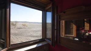 A room with a large window overlooking a barren landscape with sparse vegetation and distant hills.