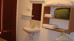 Ein Hotelzimmer mit Bett, Waschbecken, Spiegel, Handtuchhalter und Ablagefläche mit gefalteten Handtüchern.