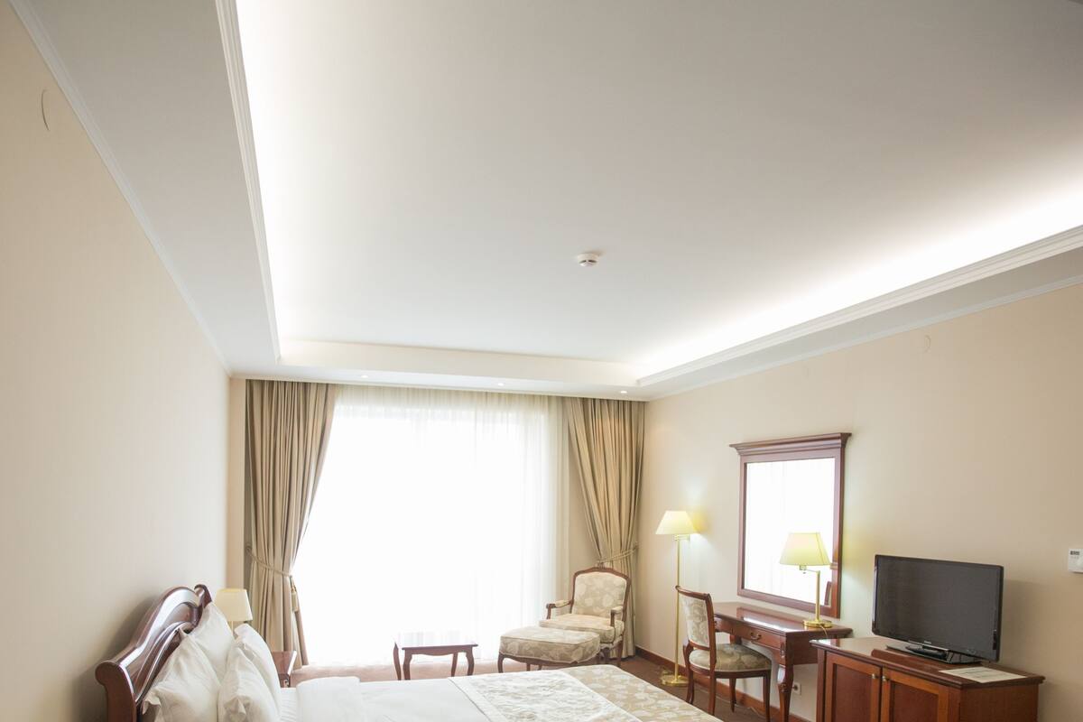 A hotel room with a bed, a desk with a television, a chair, and a window with curtains.