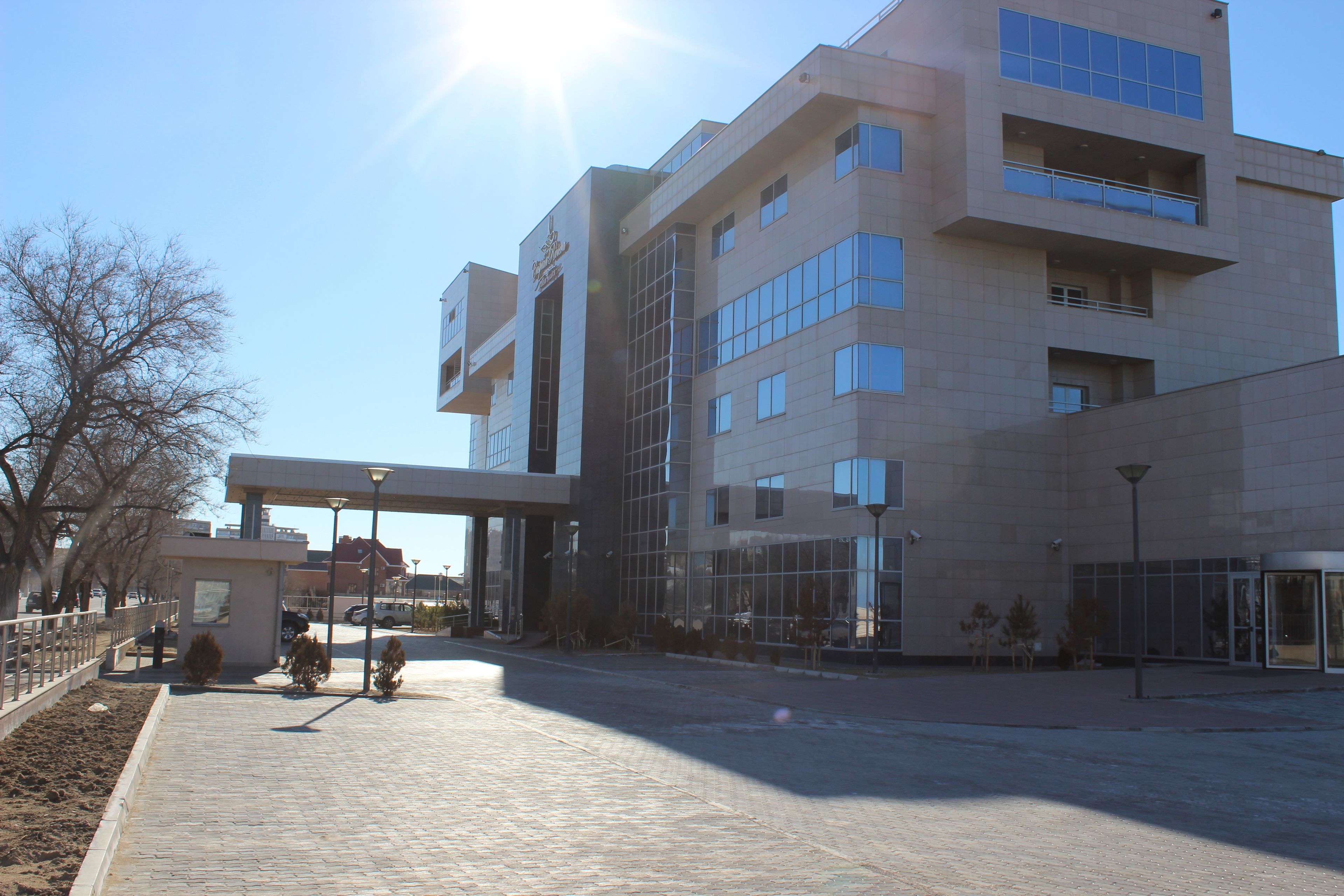 Un edificio moderno con fachada de vidrio, un acceso cubierto y una zona pavimentada con bancos.