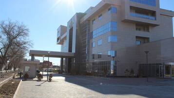 Un edificio moderno con fachada de vidrio, un acceso cubierto y una zona pavimentada con bancos.