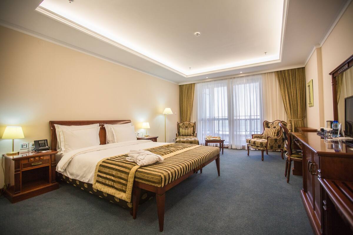 A hotel room with a large bed, two bedside tables with lamps, a chair, a desk, and a television.