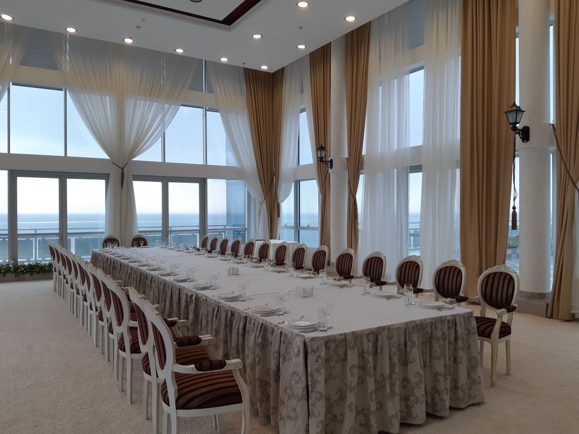A conference room with a long table set for a meeting, large windows, and curtains.
