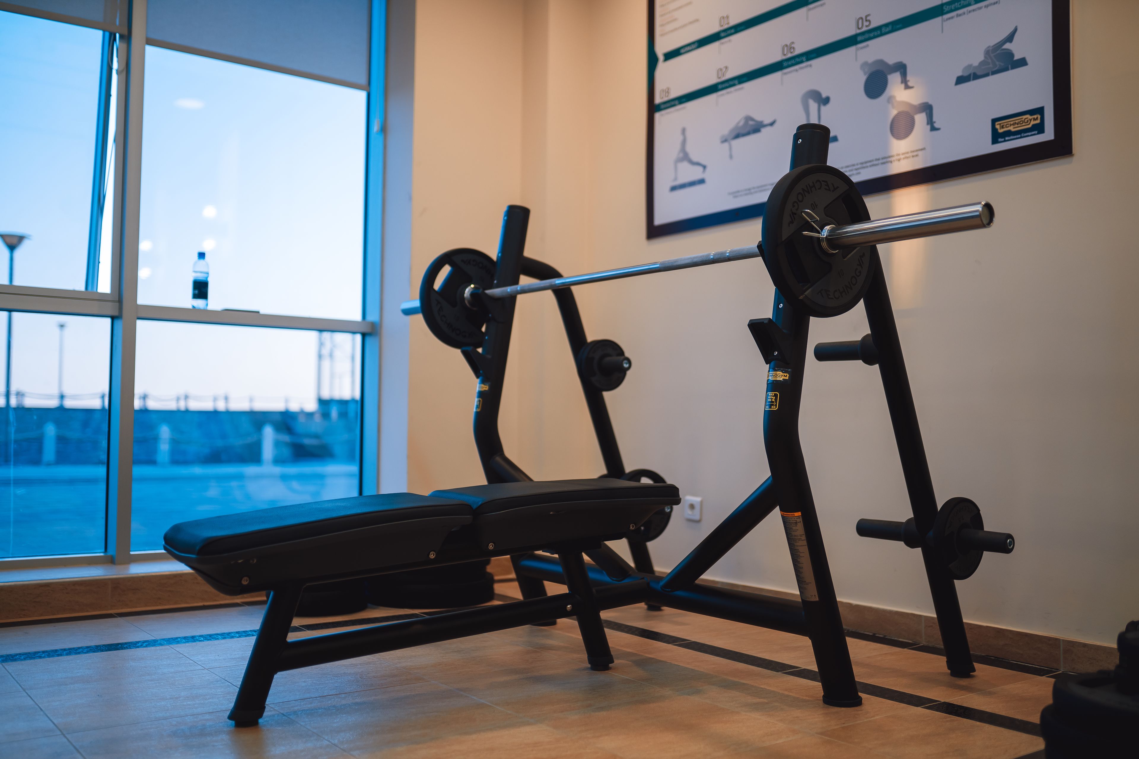 A gym with a bench press, a squat rack, and a wall-mounted poster.