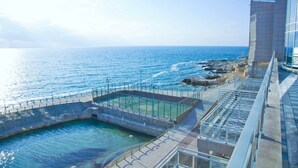 Een zwembad aan de kust met helderblauw water, een glazen balustrade en uitzicht op de oceaan.
