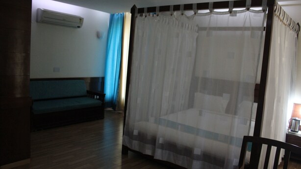 Una habitación con una cama cubierta por una cortina translúcida, piso de madera, un sofá y una mesita con una lámpara.