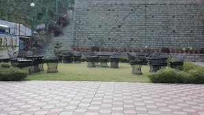 Un espacio al aire libre pavimentado con un muro de ladrillo, sillas de metal y plantas en macetas.