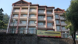 Un edificio de varios pisos con balcones, un letrero que dice Chander Mukhi Resorts y un letrero de 'No Estacionar'.