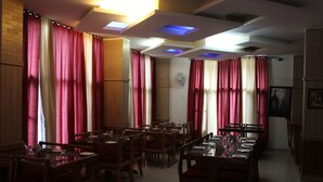 Un restaurante con varias mesas y sillas, cortinas rojas y blancas, e iluminación empotrada en el techo.