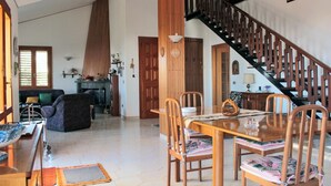 A spacious living area with a wooden dining table, chairs, and a staircase leading to an upper level. - Magma Guest House (Ragalna)