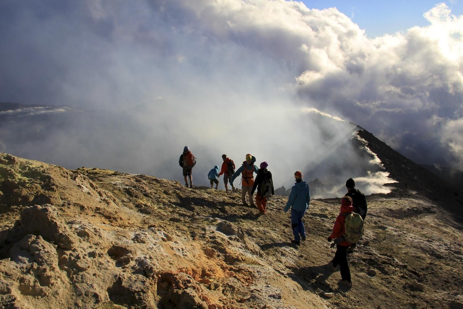 A group of hikers on a rocky mountain trail with a view of clouds and mist.