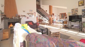 A spacious living room with a fireplace, a staircase, and a television. - Magma Guest House (Ragalna)