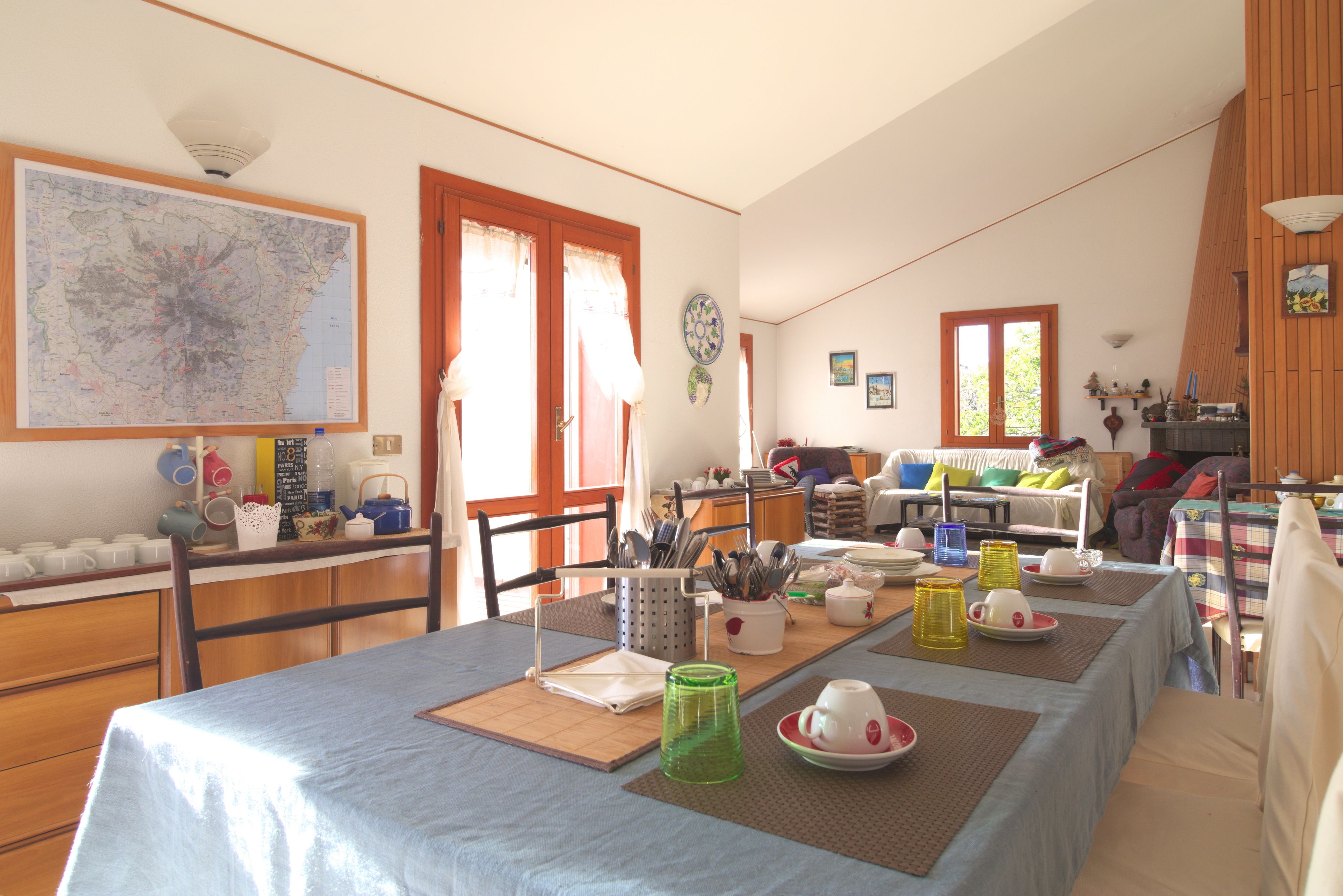 Un comedor con una mesa dispuesta para cuatro personas, un mapa en la pared y una cocina al fondo.