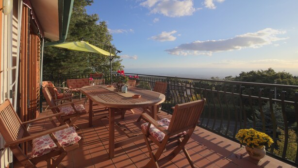 A terrace with a round table and chairs, a yellow umbrella, and a view of the sea. - Magma Guest House (Ragalna)