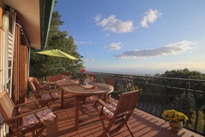 A terrace with a round table and chairs, a yellow umbrella, and a view of the sea. - Magma Guest House (Ragalna)