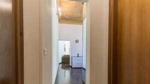 Un pasillo estrecho con puertas de madera a ambos lados, que conduce a una habitación con cama y mesita de noche.