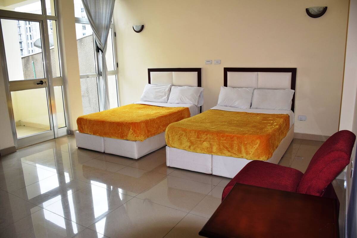 A hotel room with two beds, a red chair, and a view of the outside.