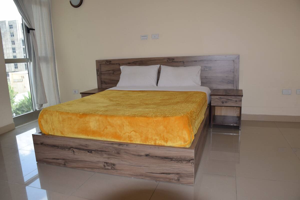 A bedroom with a wooden bed frame, a yellow bedspread, white pillows, and a nightstand.