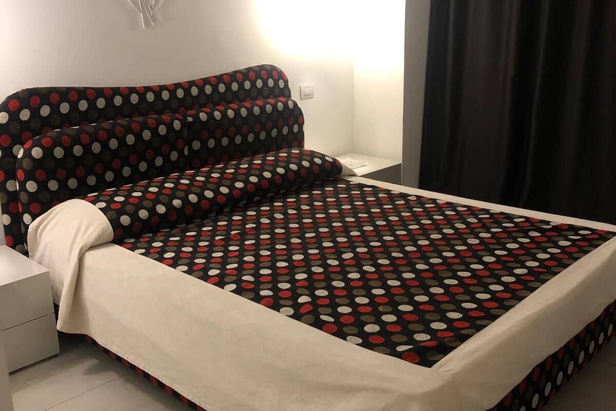 Una cama con colcha de lunares, una mesita de noche y una lámpara de pared.