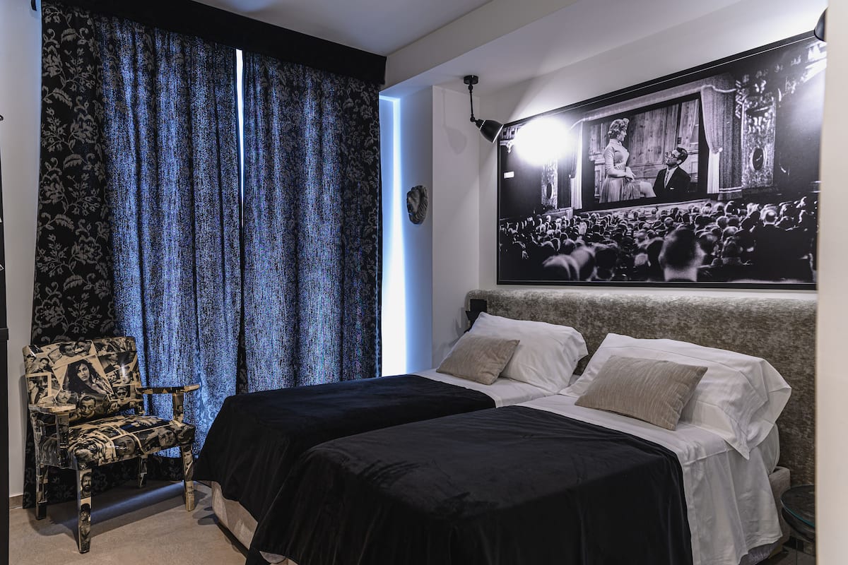 Una habitación con dos camas, un sillón estampado y un cuadro grande en la pared.