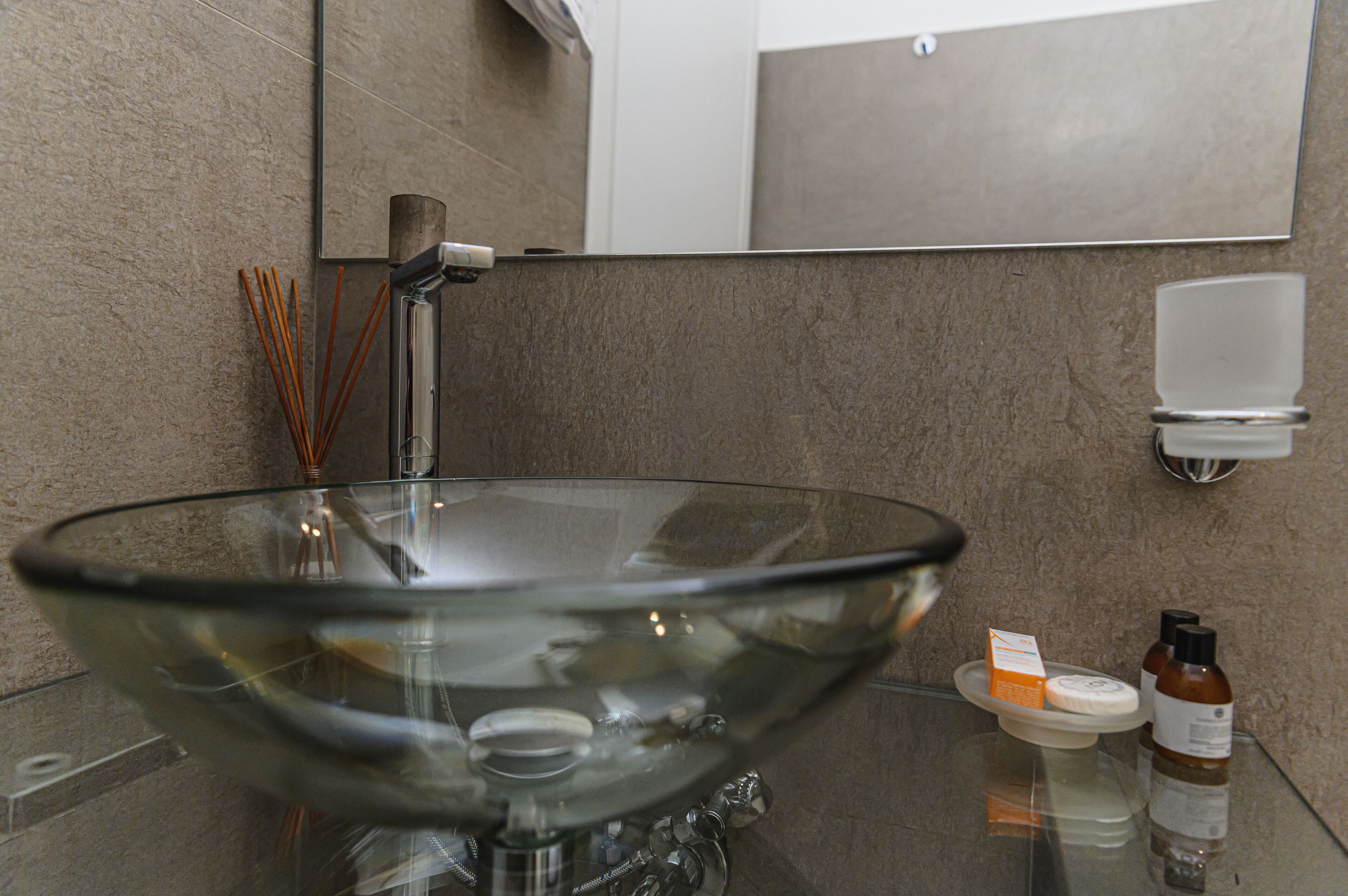 Ein modernes Badezimmer mit einem Waschbecken aus Glas, einem Spiegel und einer Seifenspender.