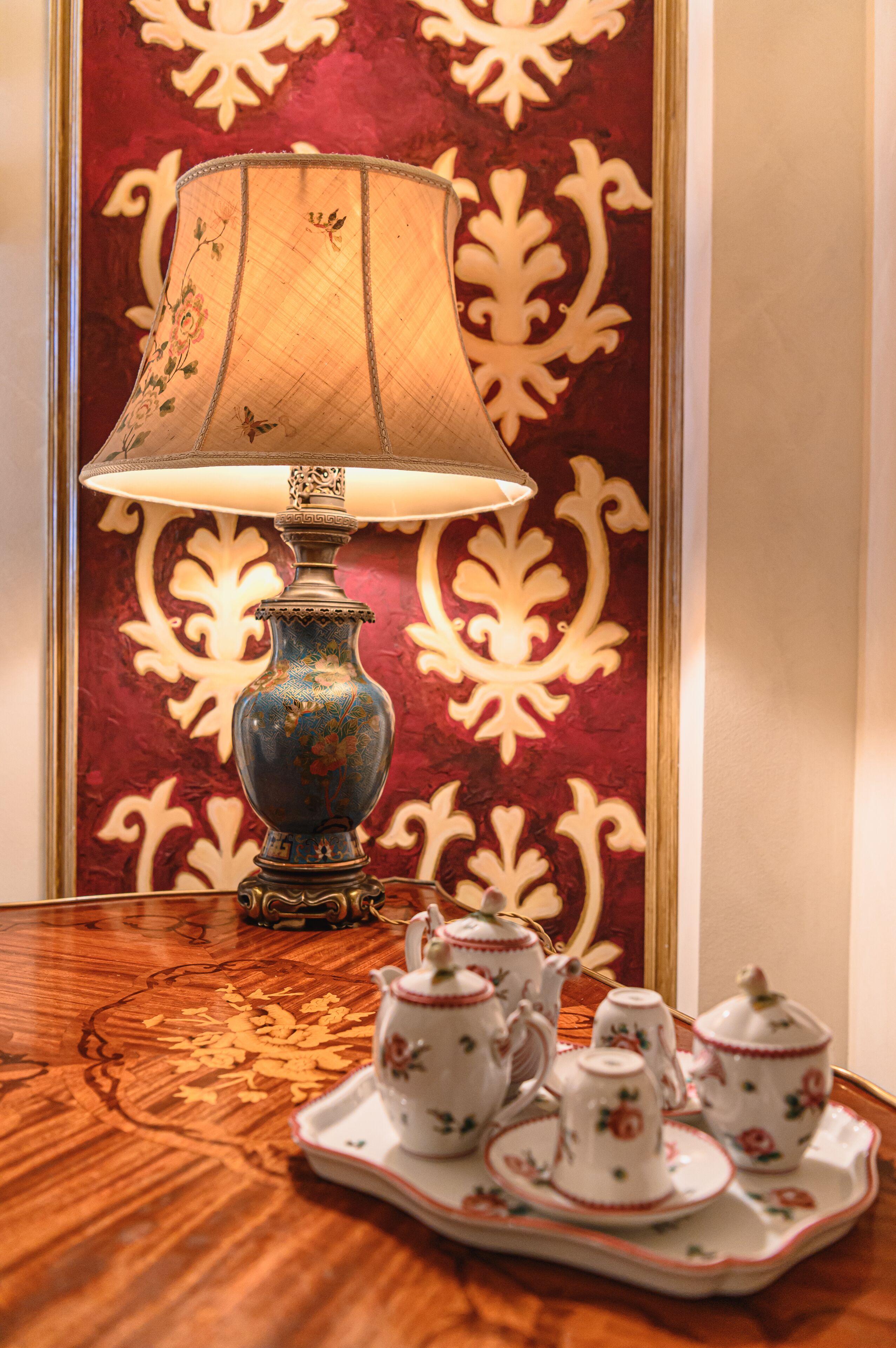 Ein Tisch mit einer dekorativen Lampe, einem Tablett mit Teetassen und einer Wand mit Blumenmuster.