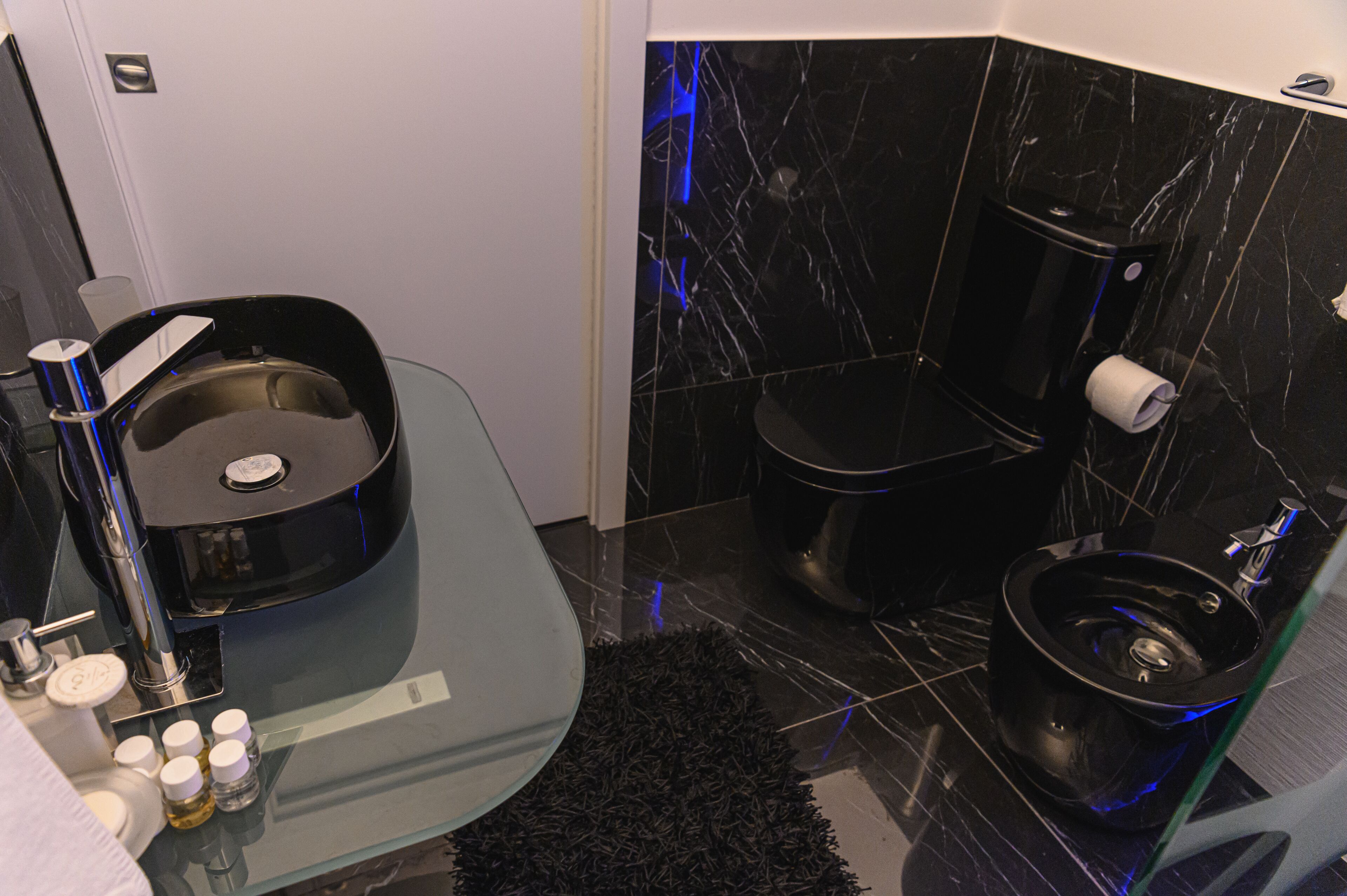 Un baño moderno con lavamanos de cristal, inodoro negro y suelo de mármol.