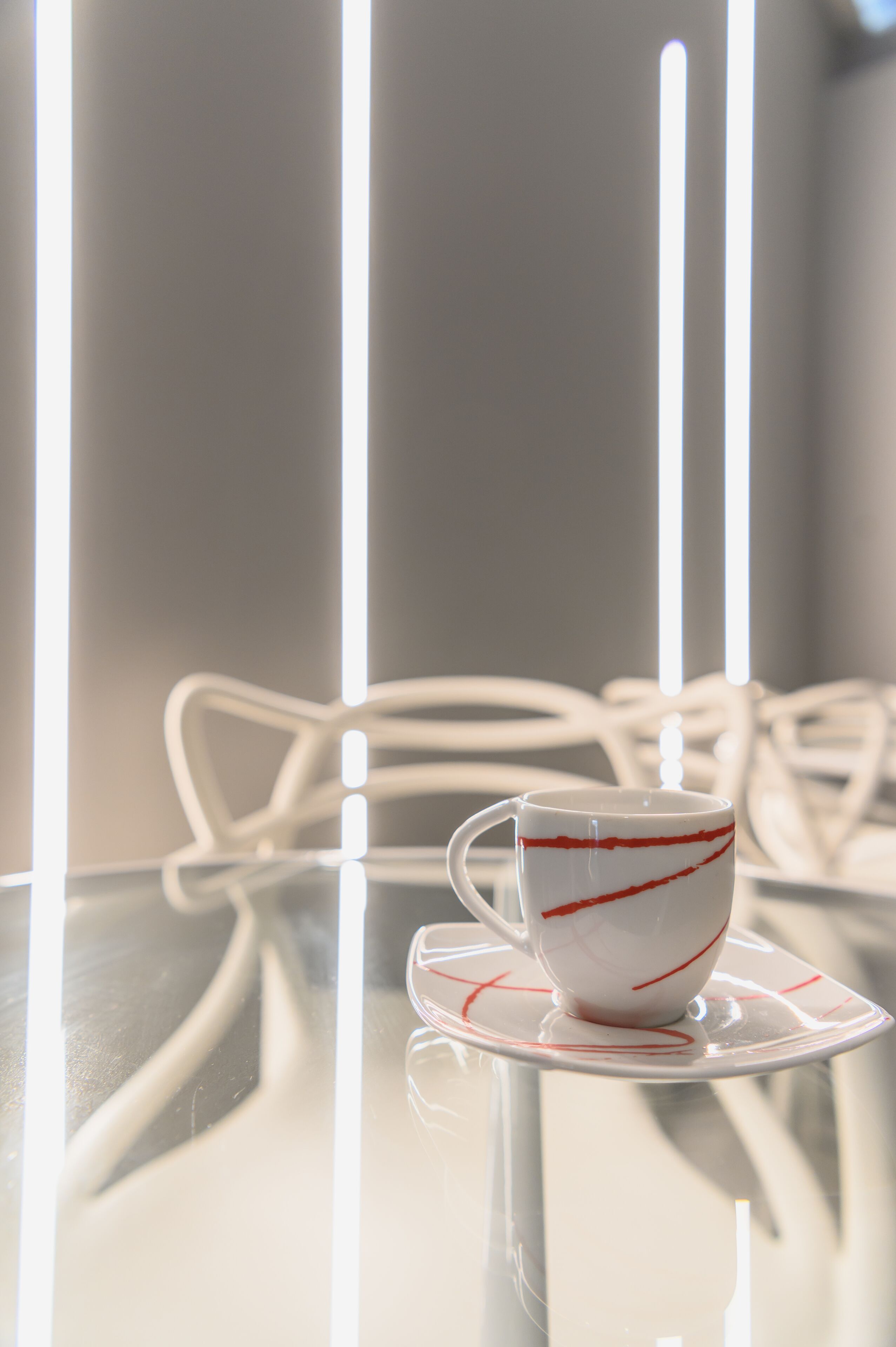 Een witte kop met rode strepen op een schotel, geplaatst op een glazen tafel met een reflecterend oppervlak.