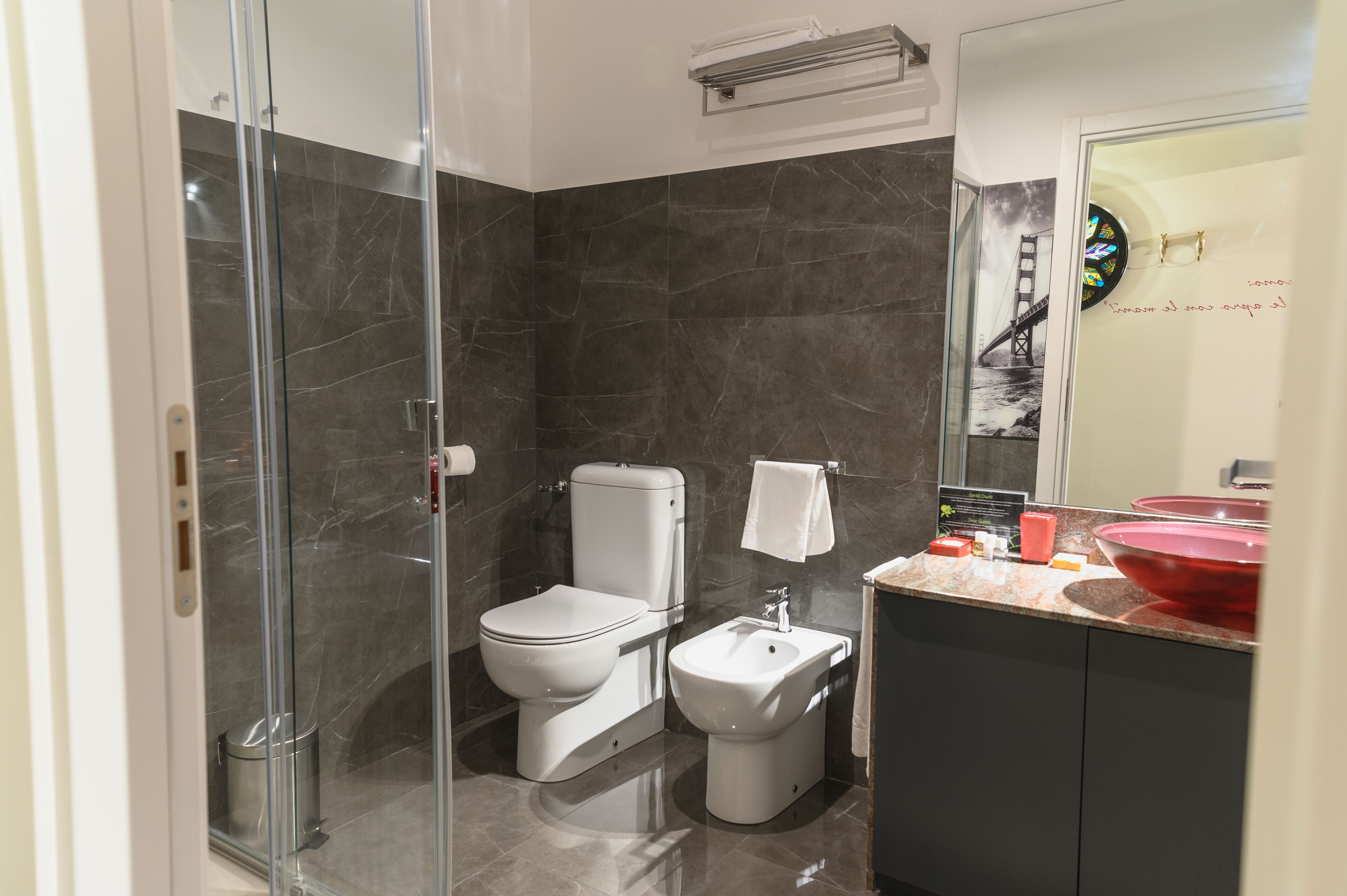 Ein modernes Badezimmer mit einer Duschkabine aus Glas, Toilette, Bidet und einem Waschtisch mit rotem Becken.
