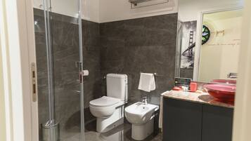 Ein modernes Badezimmer mit einer Duschkabine aus Glas, Toilette, Bidet und einem Waschtisch mit rotem Becken.