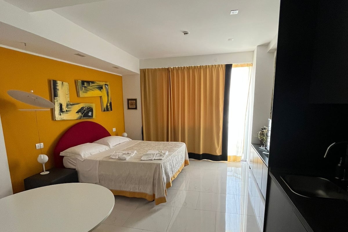 Una habitación de hotel moderna con cama, mesa de comedor y zona de cocina.
