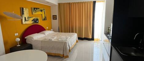 A modern hotel room with a bed, a dining table, and a kitchen area.