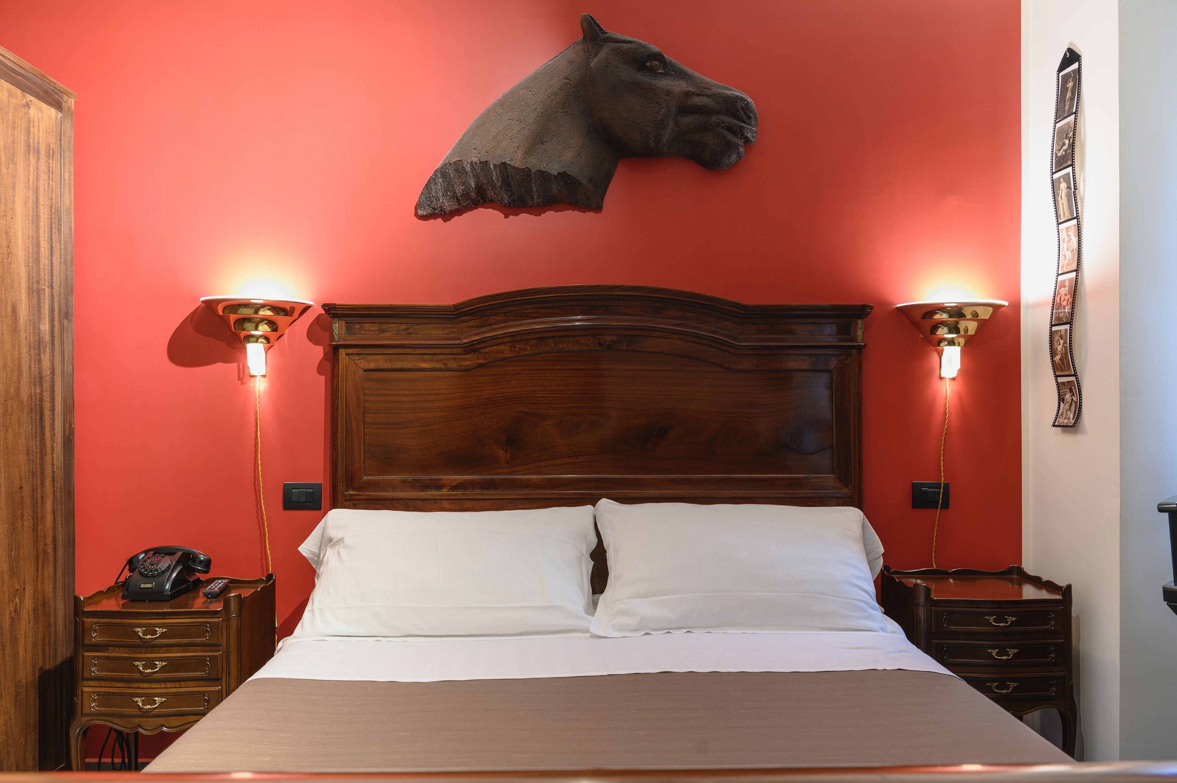 Un dormitorio con cabecera de madera, dos mesitas de noche con lámparas, un teléfono y una pared roja.