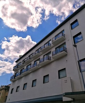 En flervåningsbyggnad med balkonger, stora fönster och en klar himmel med moln.