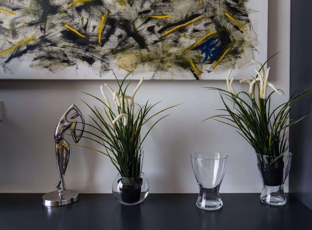 Tres plantas en macetas sobre una mesa, con un cuadro abstracto grande al fondo.