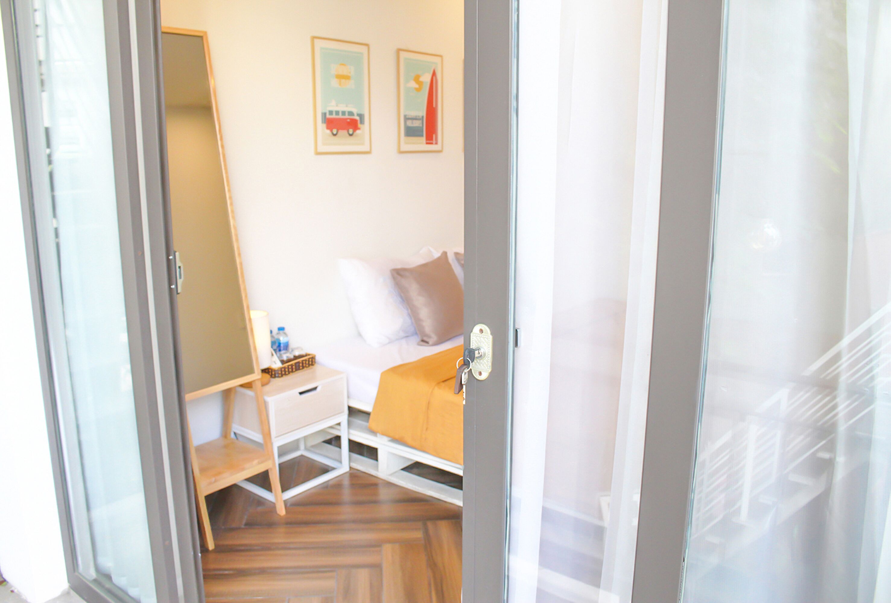 A room with a bed, a bedside table, a chair, and a small desk. There are two framed pictures on the wall.