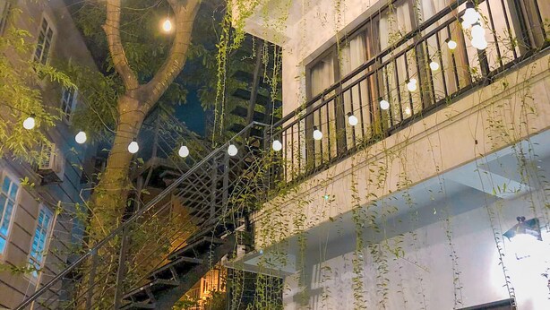 Een meerlaags gebouw met buitentrap, lichtslingers en hangende planten.