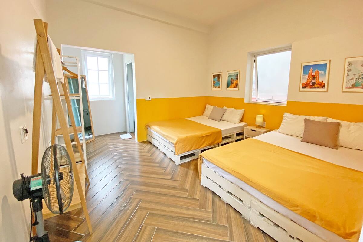 A room with two beds, a ladder, and a fan. There are two windows and a door.