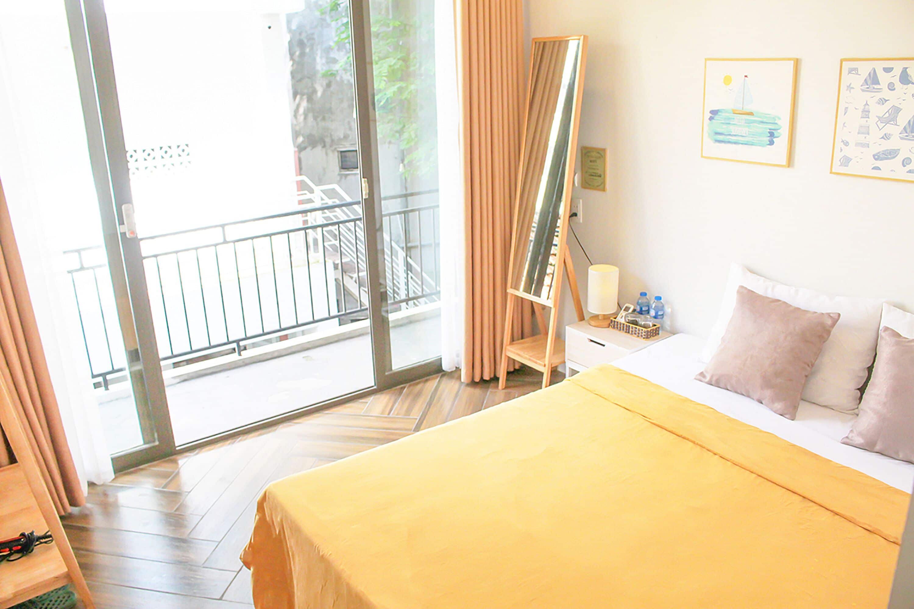 A hotel room with a bed, a nightstand, a mirror, and a view of a balcony.