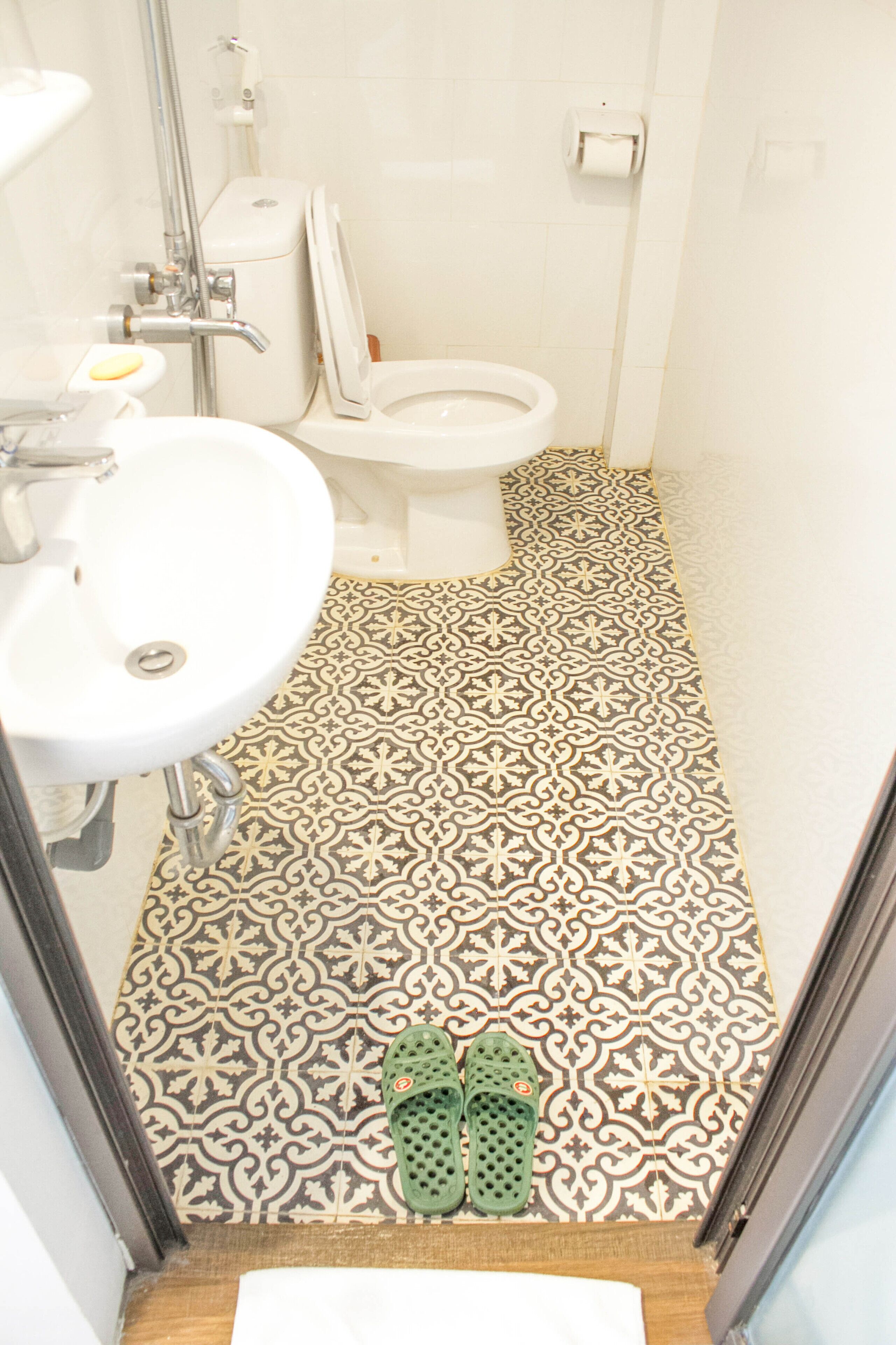 Une salle de bain avec un lavabo blanc, des toilettes et des carreaux de sol à motifs.