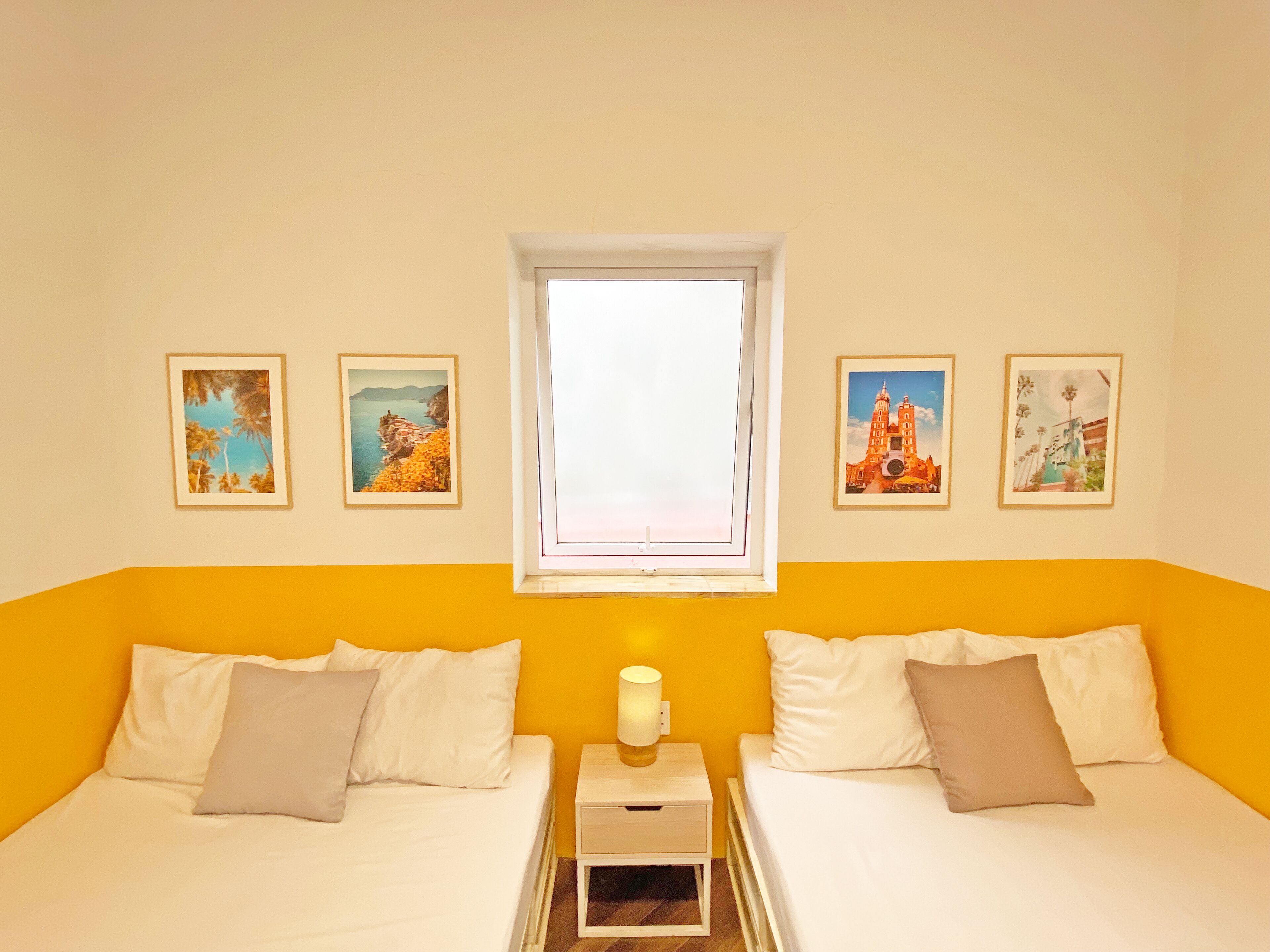 Ein Zimmer mit zwei Betten, einem Fenster und vier gerahmten Bildern an der Wand.