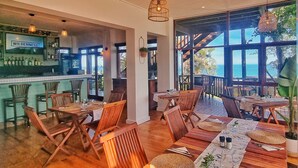 A restaurant with wooden furniture, a bar area, and large windows offering a view of the sea. - Boardwalk Lodge - B&B (Wilderness)