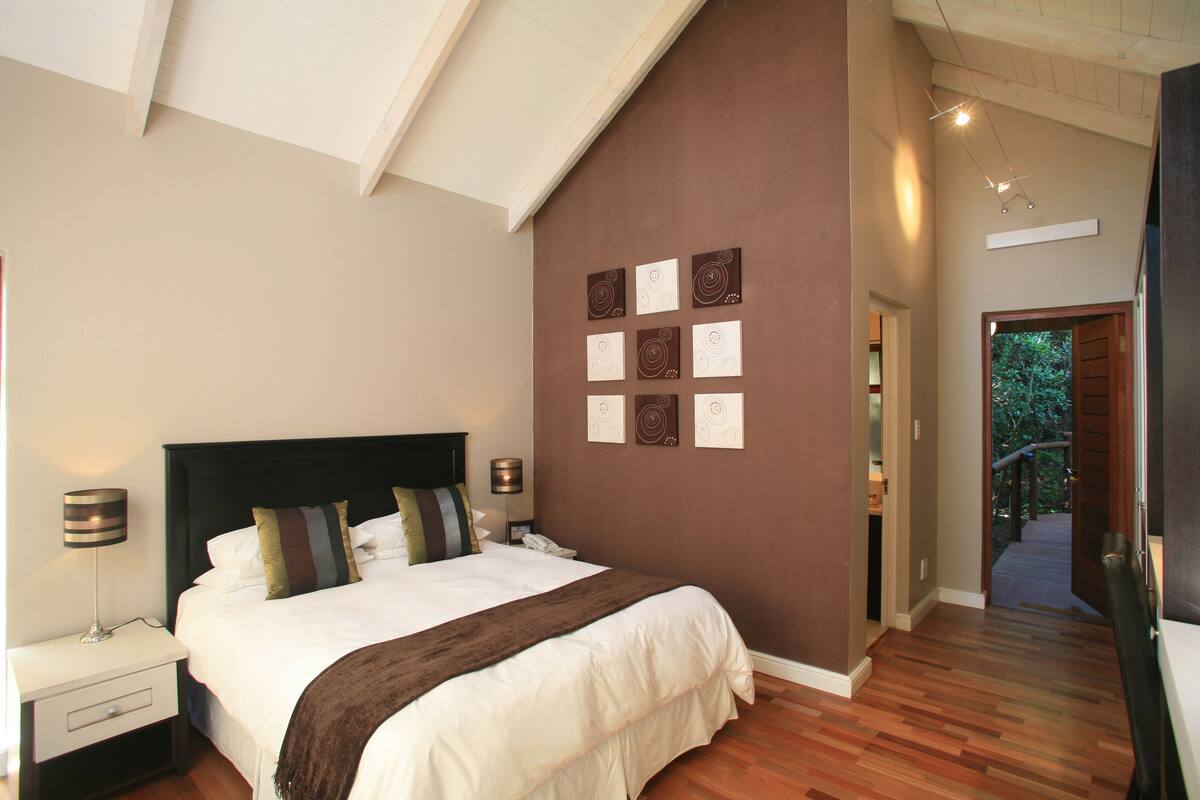 A bedroom with a large bed, a nightstand, a lamp, and a wall with decorative plates.