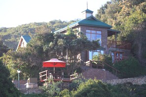A stone building with a green roof, a wooden deck, and a red umbrella. - Boardwalk Lodge - B&B (Wilderness)