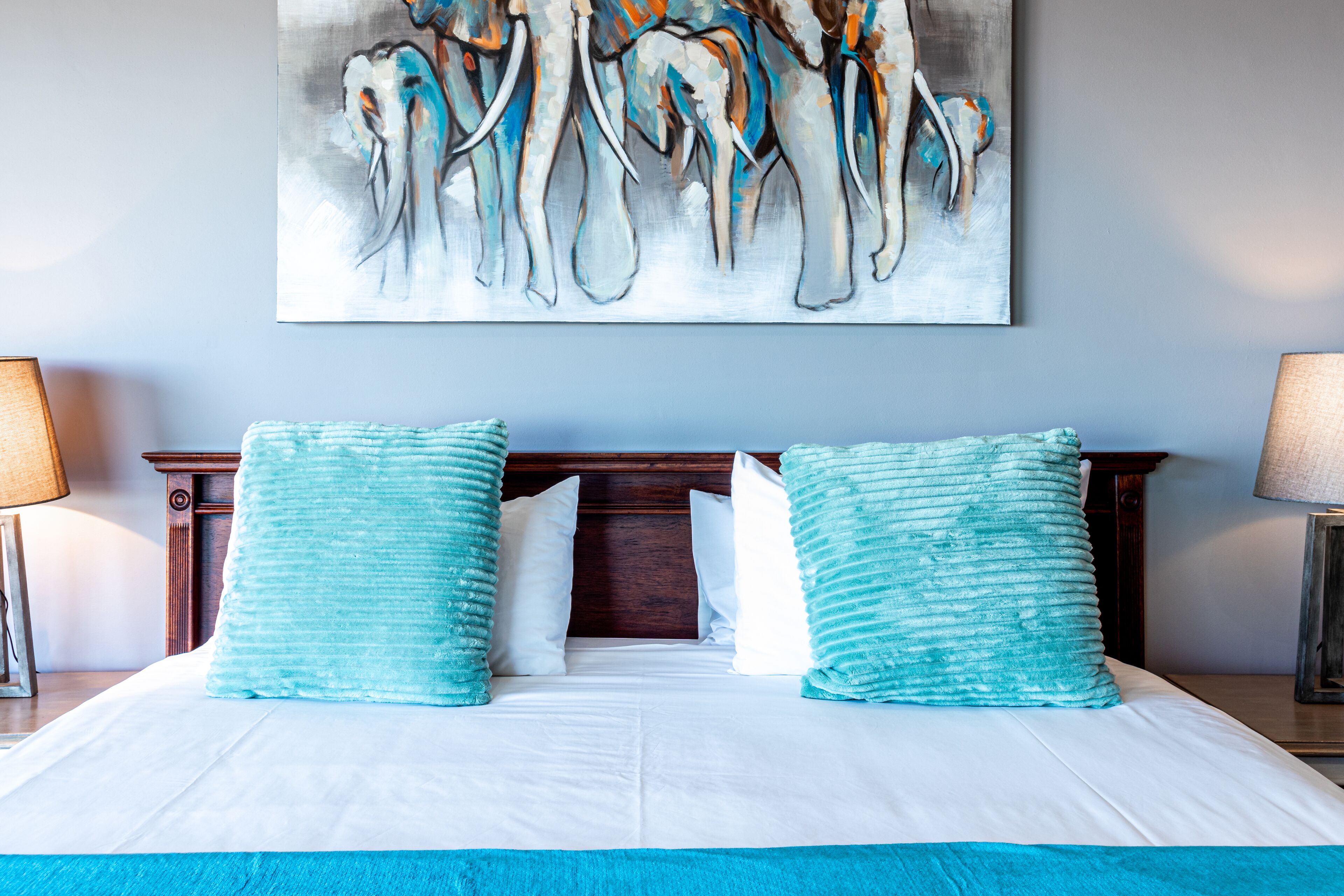 A hotel room with a large bed, two matching pillows, a wooden headboard, and a painting above the bed.