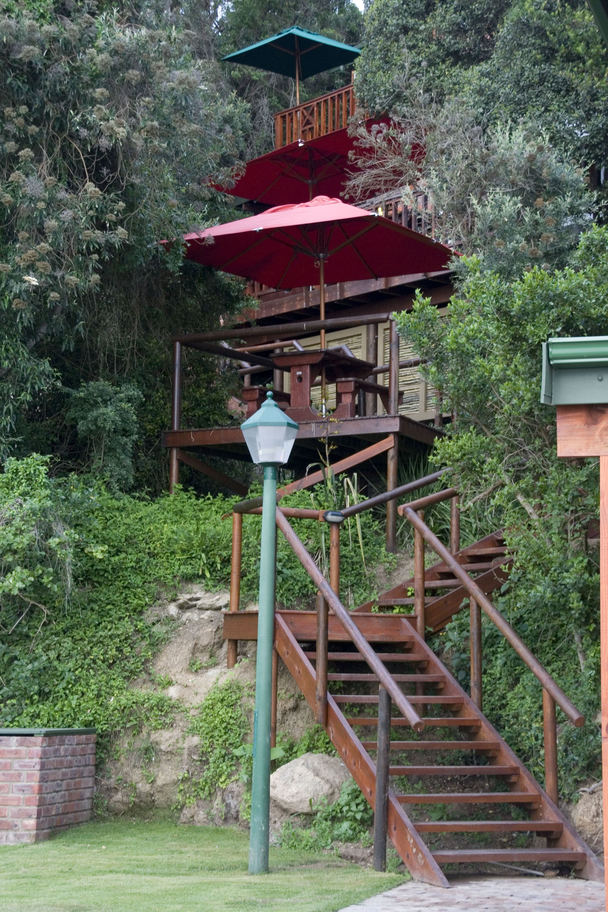 A wooden staircase with a metal railing leading to a platform with a red umbrella.