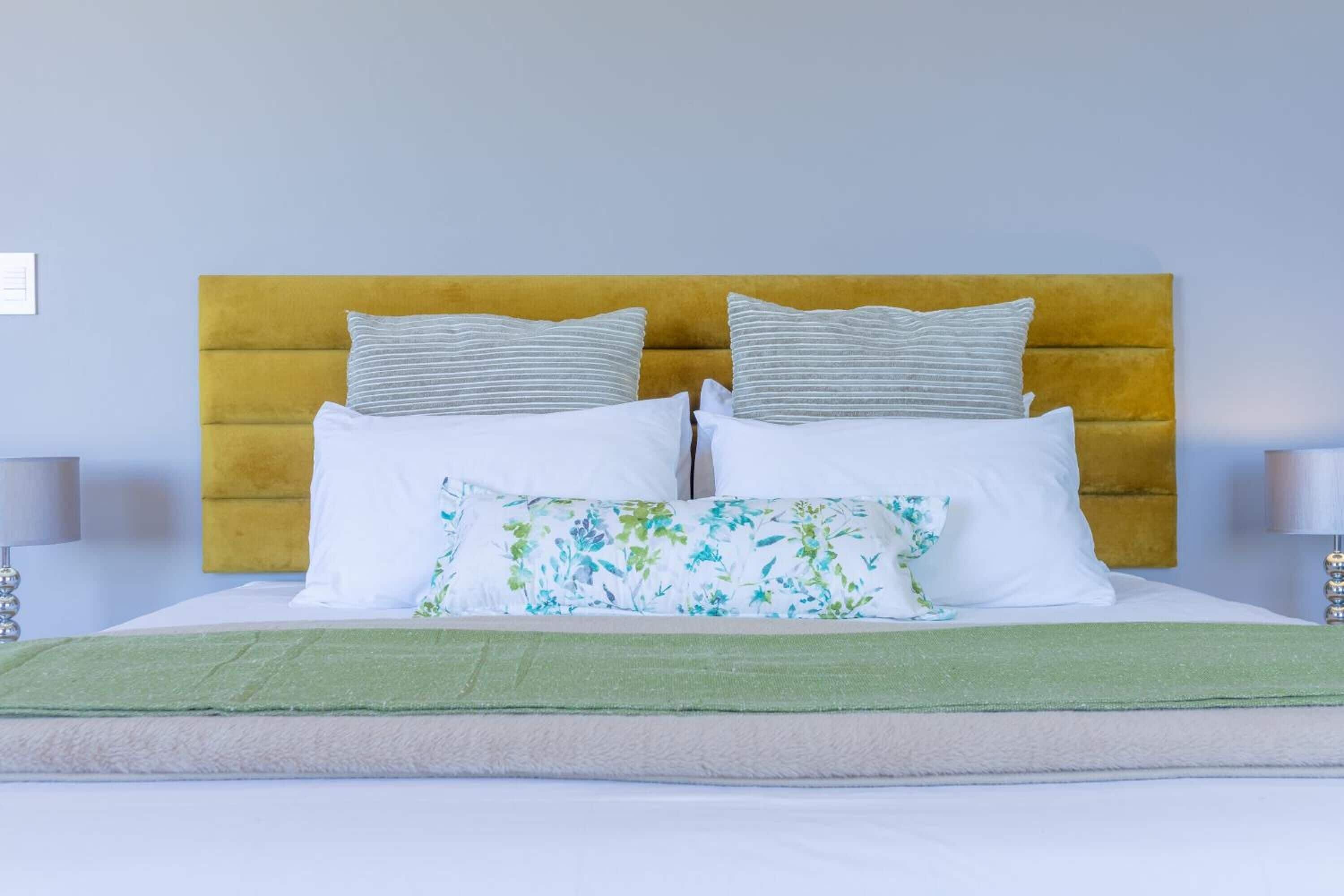Una cama bien tendida con un plaid verde, un cabecero amarillo y dos lámparas de noche.